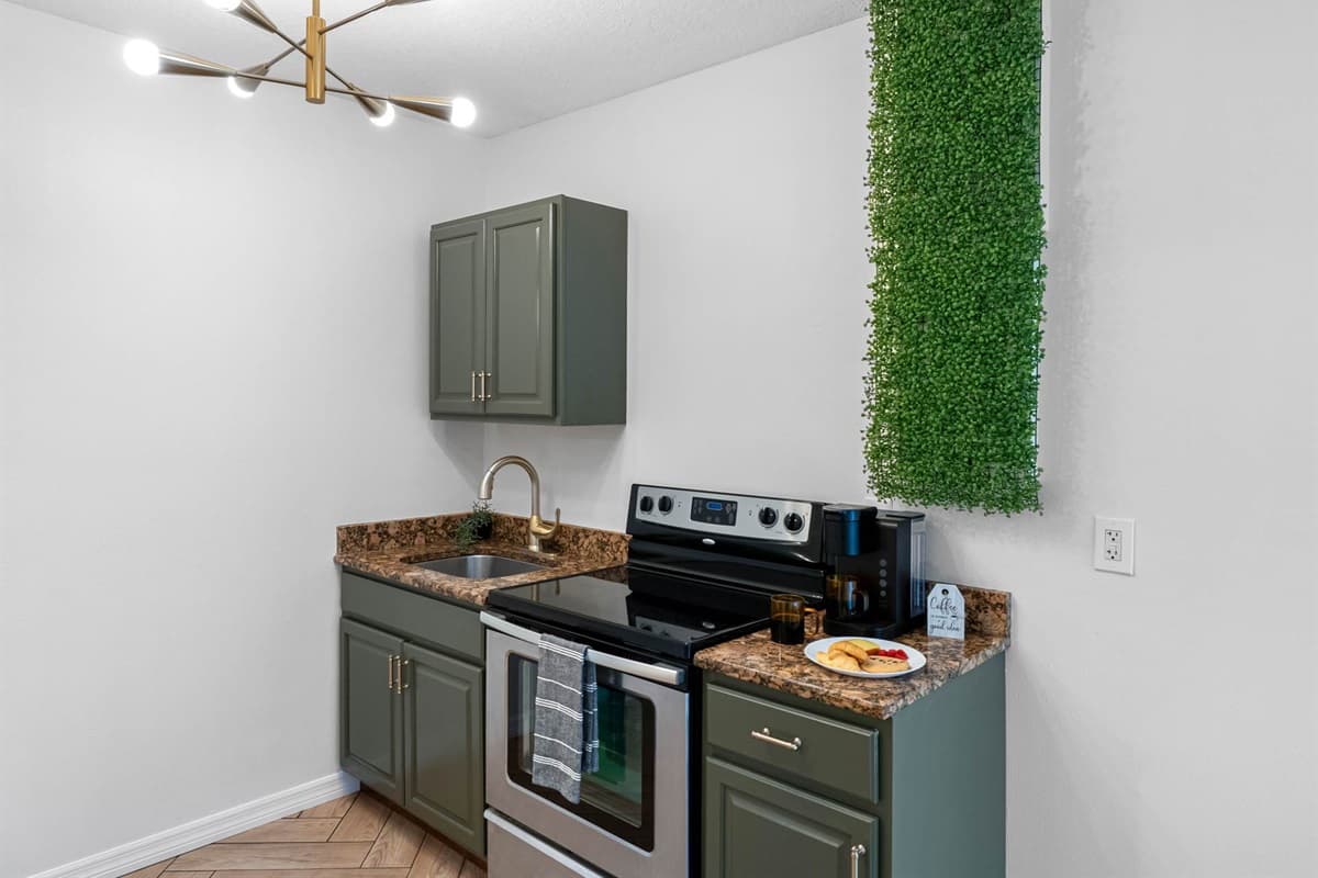 Featuring a sleek stainless steel stove, granite countertops, and olive green cabinetry, this space is both functional and visually inviting.