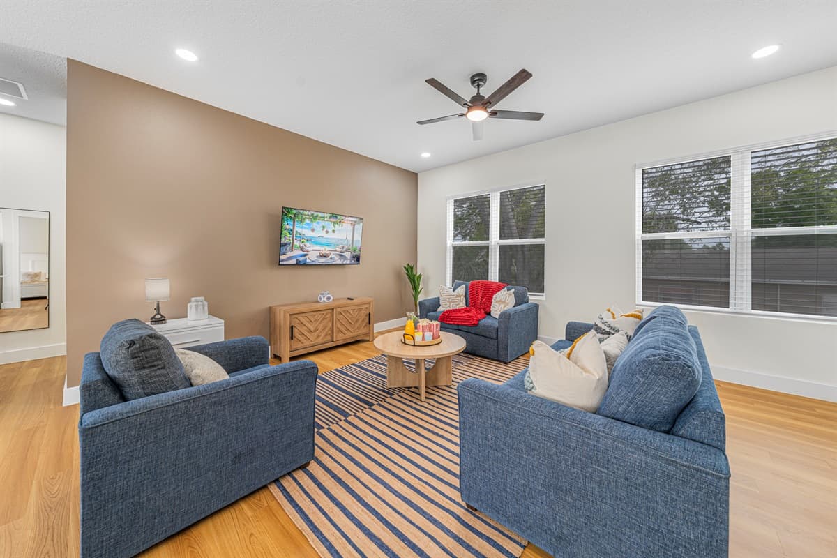 Oversized windows flood the living room with natural light while the ceiling fan keeps the Florida air perfectly comfortable.